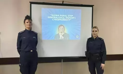 Dwie policjantki stojące przed ekranem wyświetlającym temat spotkanie. 